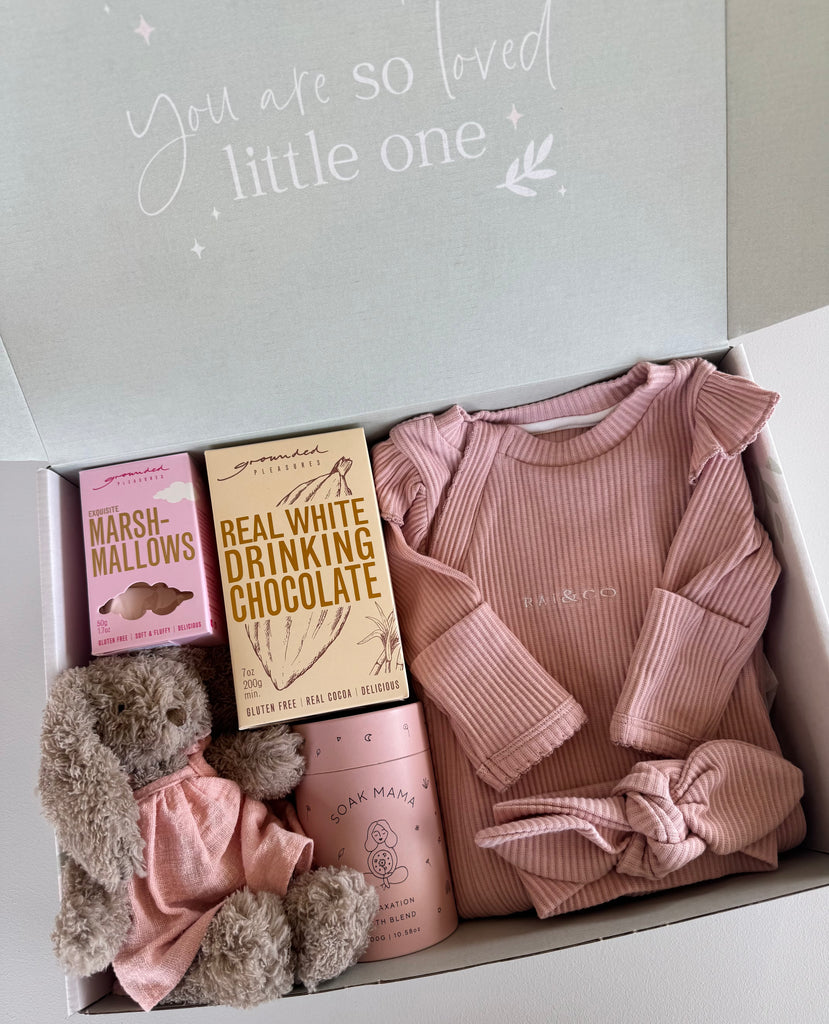 Baby gift set with pink baby clothes, chocolate, and a teddy bear in a box.