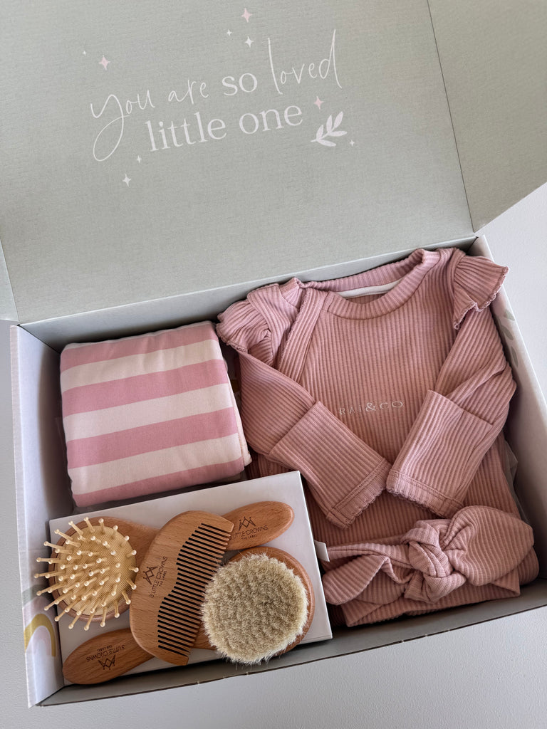 Baby gift set with pink clothes, striped blanket, and baby care items in a box.