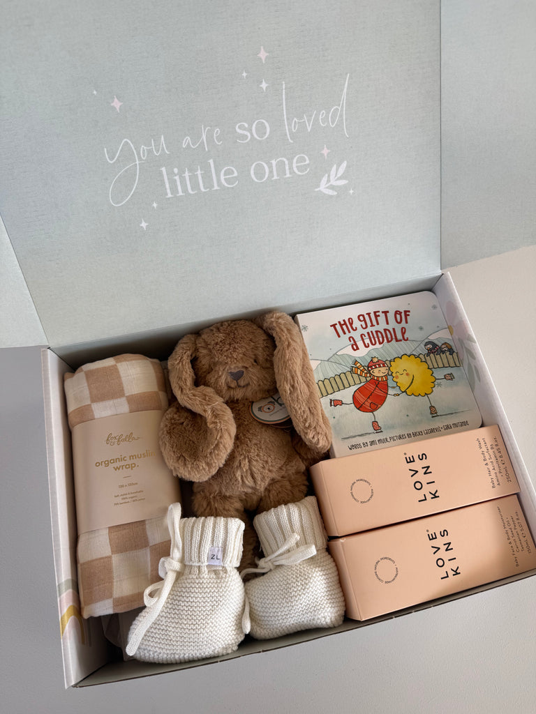 Baby gift set with teddy bear, blanket, booties, and book in a box with 'You are so loved little one' text.